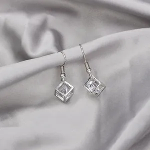 Detail view of geometric silver earrings with cubic zirconia on silk fabric background
