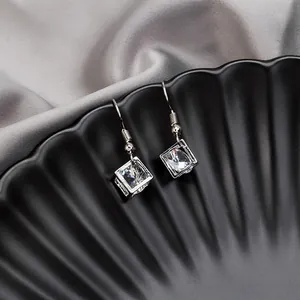 Close-up of silver tassel earrings with hollow cube design and clear square crystals
