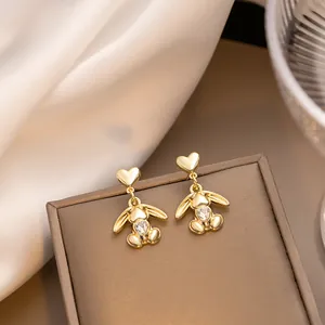 Detail of golden bunny tassel earrings with heart zircon inlay on a soft silk background
