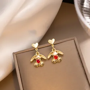 Close-up of gold tassel earrings featuring a cartoon bunny and red heart-shaped gemstone