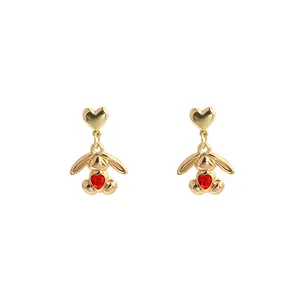 Detail of golden rabbit tassel earrings with red heart gemstone and polished finish