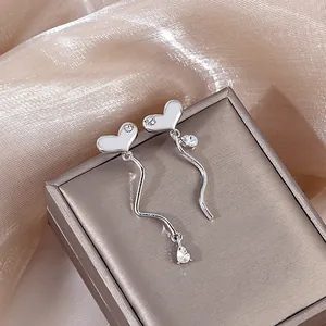 Detailed shot of silver heart tassel earrings with crystals on luxury silk fabric