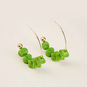 Detailed shot of golden hoop earrings featuring five green cubic textured beads