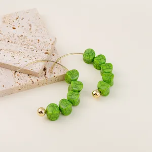 Detail of green textured beads on gold hoop earrings with bohemian stone patterns