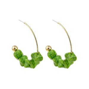 Detail of bohemian gold hook earrings featuring vibrant green textured resin beads