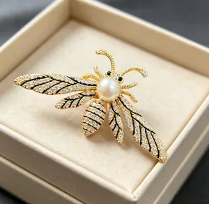 Macro shot of bee brooch featuring white pearl, sparkling rhinestones and gold plating