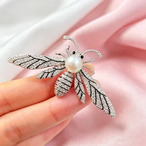 Elegant bee brooch with sparkling crystals and large pearl held by hand on silk