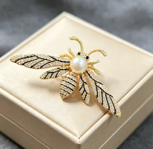 Close-up of golden bee brooch featuring white pearl and sparkling crystals on jewelry box