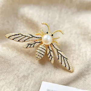 Elegant gold bee brooch with sparkling crystals and a white pearl on fabric background