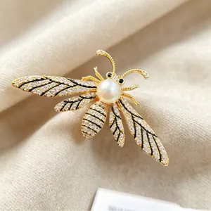Elegant gold bee brooch with white pearl and sparkling crystals on a textured fabric background