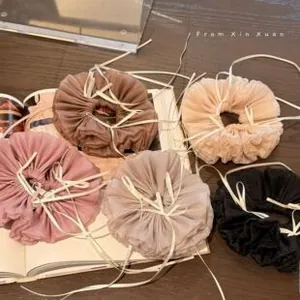 Detail of five organza hair scrunchies with white ribbons on a wooden background
