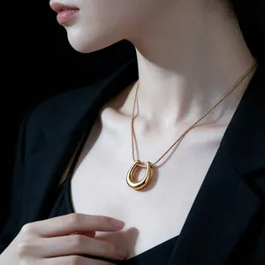 Close-up of a golden horseshoe pendant necklace worn by a model in a black suit