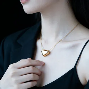 Close-up of a polished golden heart pendant on a delicate chain around a model's neck