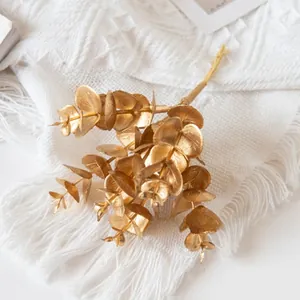 Detailed view of artificial golden eucalyptus leaves on a textured white fringe blanket