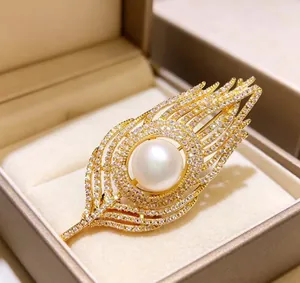 Detailed view of elegant gold feather brooch with crystals and a large white pearl center