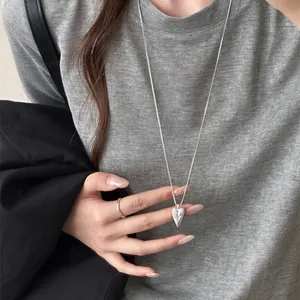 Detail shot of silver pointed heart pendant necklace with engraved pattern on grey shirt