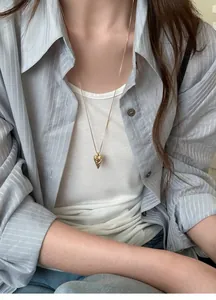 Detailed view of a gold pointed heart pendant necklace with totem texture on a model.