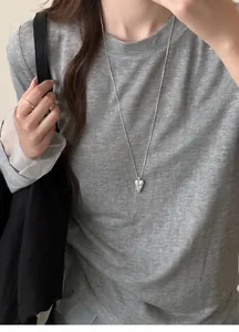 Detailed view of a silver heart pendant necklace on a grey t-shirt, elegant design