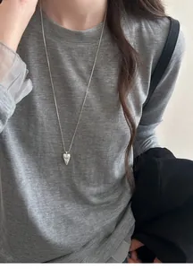 Detail view of a stylish silver pointed heart totem necklace worn on a grey knit sweater