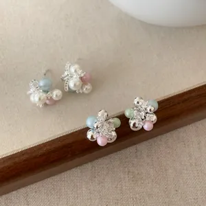 Eleganti orecchini a lobo con perle pastello e cristalli in un ambiente naturale.