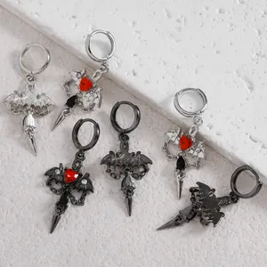 Gothic earring set featuring bat wings, red heart gems, and spikes on stone surface