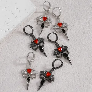 Macro detail of gothic earrings with red hearts, bat wings, and dagger-shaped pendants