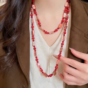 Detail view of a long red glass bead and faux shell beaded necklace worn on a model