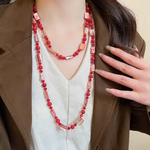 Detail shot of red glass bead and faux shell necklace worn over a brown blazer.