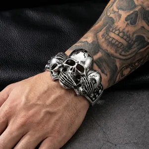 Detail of retro punk stainless steel cuff featuring three skull motifs in silver finish