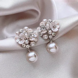 Close-up of elegant French flower earrings featuring zircons and drop pearls on silk background