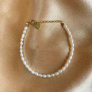 Macro detail of Baroque freshwater pearl bracelet with gold heart charm on silk fabric