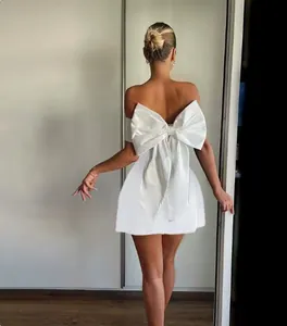 Macro detail of the oversized bow decoration on the back of the white satin mini dress