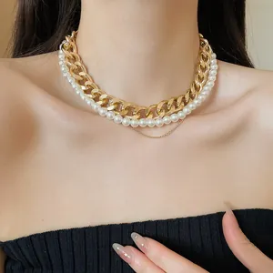 Detail view of stylish layered gold curb chain and white pearl necklace on model