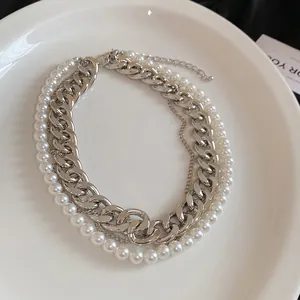 Detail view of a multi-layer chunky silver chain and pearl necklace on a white plate.