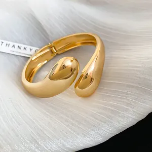 Macro view of a chunky gold-plated open bracelet resting on elegant white pleated fabric.