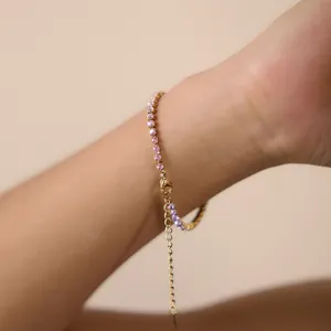 Dettaglio ravvicinato di un bracciale dorato in acciaio con zirconi colorati sfumati al polso.