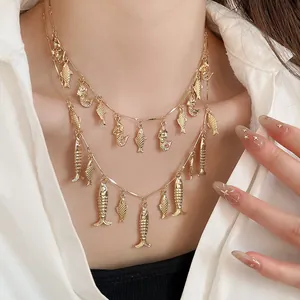 Primer plano de un collar dorado de dos capas con colgantes de peces detallados en una modelo.