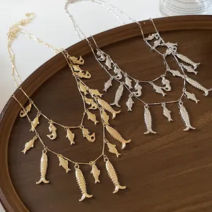 Primer plano de collares de doble capa en oro y plata con colgantes de peces sobre bandeja