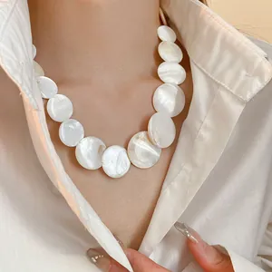 Macro view of an elegant white shell round disc necklace worn with a white shirt