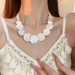 Detailed view of a white round shell geometric necklace worn with a seaside outfit