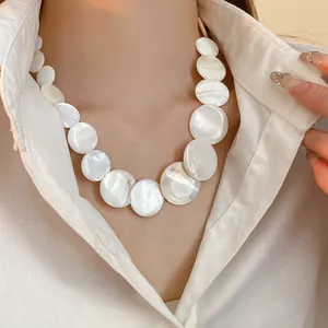 Close-up of a white circular shell disc necklace on a white shirt background