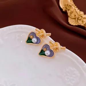 Boucles d'oreilles cœur élégantes avec émail violet, perles et détails de nœud dorés.