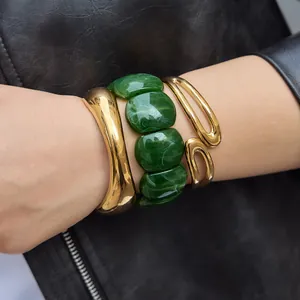 Close-up of chunky green marbled resin bracelet paired with gold bangles on wrist