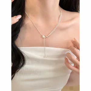 Dettaglio di una collana lariat d'argento minimalista con un ciondolo a cuore su modella.