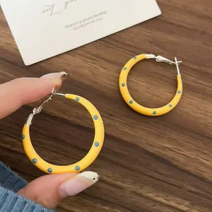 Close-up detail of stylish yellow enamel hoop earrings featuring blue polka dots