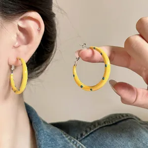 Macro detail showing yellow enamel hoop earrings with blue polka dots on ear and held.
