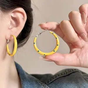 Detail of yellow polka dot hoop earrings held by hand and worn on ear