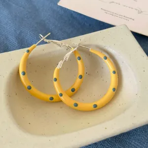 Detailed macro shot of yellow hoop earrings with blue polka dots on a ceramic plate
