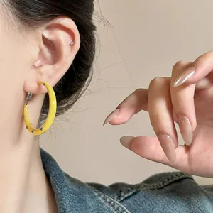 Detailed close-up view of a yellow enamel hoop earring with blue polka dots worn on ear