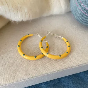 Close-up of stylish yellow hoop earrings featuring blue polka dots and silver needle posts